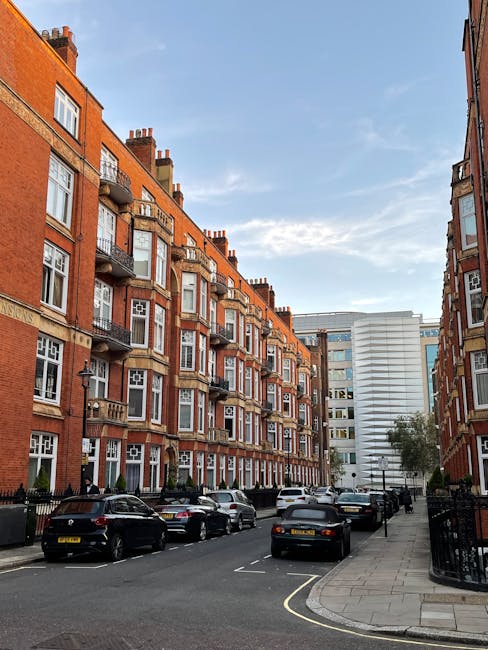 A city street scene in Knightsbridge, featuring historic and ornate buildings with detailed facades, large windows, and decorative rooftops, under a partly cloudy sky. The street is lined with parked 